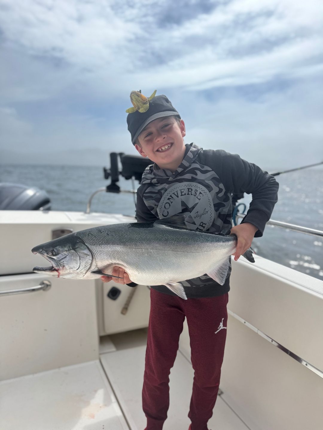 Young Child With Fish Cap Holding His Salmon In The Back Of The Boat